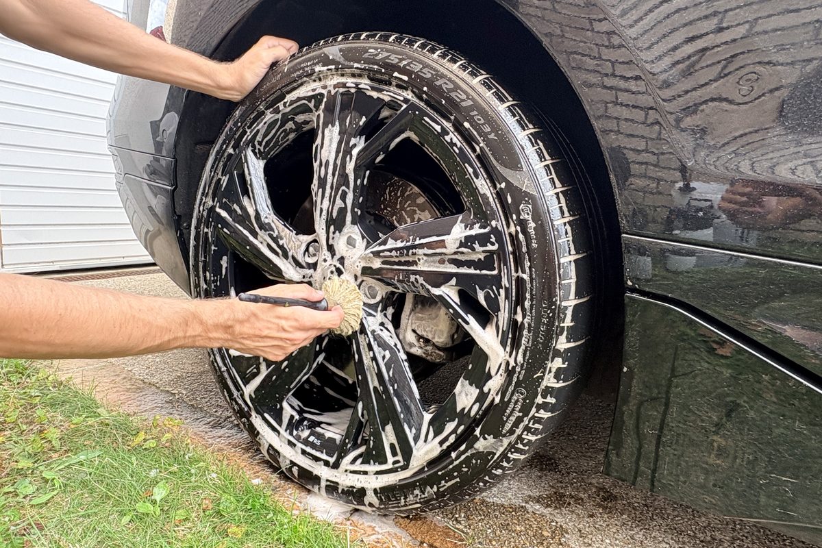 Nettoyage d'une jante de voiture à la brosse sous mousse savonneuse